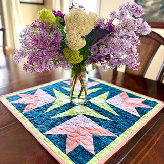 Close-up of a colorful quilted table centerpiece with floral shapes in pink, green, and blue fabric, featuring the Dancing Lilies Quilt Pattern (Download) by Shadow Valley Quilts.
