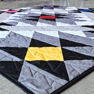 Desert Chill Quilt Pattern by Staci W Quilts closeup: angled view of grey, black, white, yellow, and red triangle and diamond blocks on a wood floor.