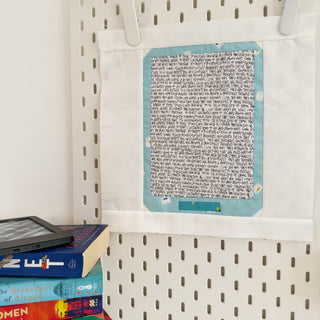E Reader Block Pattern (Download) quilt block by Lou Orth Designs, featuring a fabric design resembling an e-reader with text print and blue border, hanging for display.