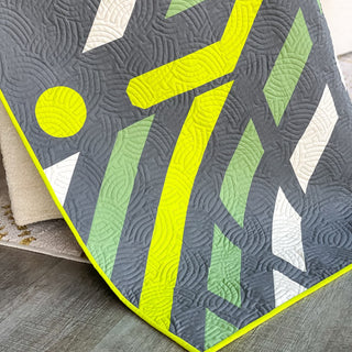 Faceoff Quilt Pattern (Download) by Jessica Steele Design featuring a modern geometric hockey quilt in charcoal lime sage and white with flowing quilting