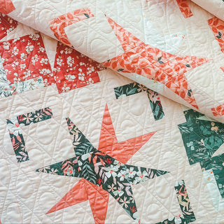 Close-up of a quilt made with floral star and geometric block patterns in soft red, green, and cream colors, showcasing detailed stitching from A Piece of Quiet Quilts using the Festive Gala Quilt Pattern (Download).