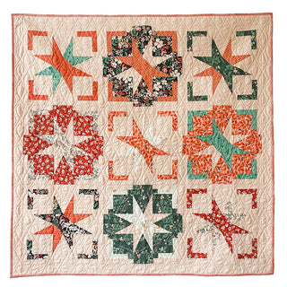 A handmade quilt in festive red, green, and cream tones featuring star and geometric patterns, showcasing the Festive Gala Quilt Pattern (Download) by A Piece of Quiet Quilts.