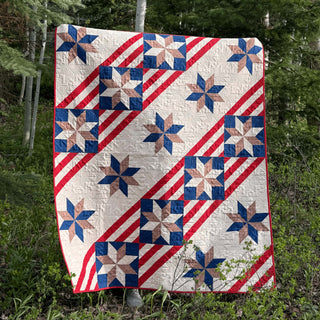 Quilt with red, white, and blue star and stripe blocks hanging outdoors, showcasing the Fifty Nifty Quilt Pattern (Download) by Shadow Valley Quilts.