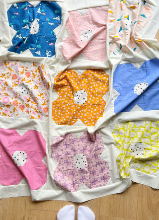 Colorful flower-shaped quilt blocks arranged on a floor showcasing the Flower Friends Quilt Pattern (Download) by Lou Orth Designs with bright, playful fabrics.