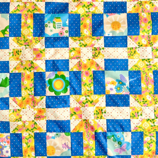 Bright colorful quilt with floral, sun, butterfly, and bird motifs in blue, yellow, and cream, showcasing the Footpath Quilt Pattern (Download) by Sewn.