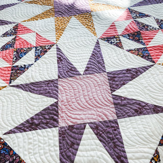 Freya June Quilt Pattern by A Piece of Quiet Quilts closeup: detailed star block with purple, pink, gold, and white triangles showing swirl quilting pattern.