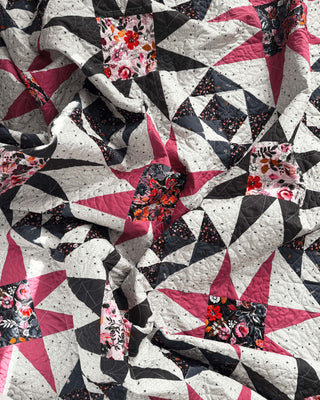 Close-up of a colorful quilt with pink, black, and floral star patterns made using the Freya June Quilt Pattern (Download) by A Piece of Quiet Quilts.