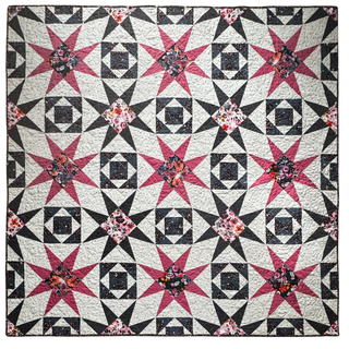 Flat-lay image of a dark-themed quilt with pink and black star blocks and floral patterns showcasing the Freya June Quilt Pattern (Download) by A Piece of Quiet Quilts.