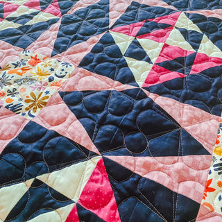 Close-up of a colorful quilt featuring geometric patterns with dark blue, pink, red, and floral fabric, showcasing detailed quilting stitches from A Piece of Quiet Quilts for Freya June Quilt Pattern (Download)