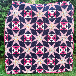 A vibrant pink and navy quilt with star and geometric block patterns made using the Freya June Quilt Pattern (Download) by A Piece of Quiet Quilts.