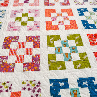 Close-up of a colorful quilt made with various patterned fabrics featuring animals and florals, created using the Front Street Quilt Pattern (Download) by A Piece of Quiet Quilts.