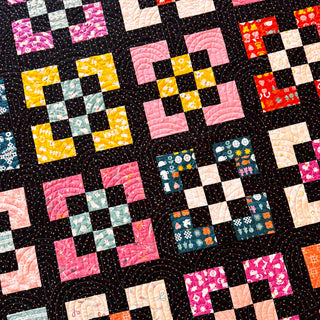 Close-up of a vibrant quilt featuring colorful geometric block patterns with floral and textured fabrics, showcasing intricate quilting from A Piece of Quiet Quilts for Front Street Quilt Pattern (Download).