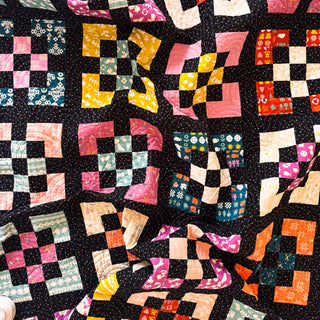 Close-up of a colorful patchwork quilt with geometric square patterns in pink, yellow, orange, green, and black, showcasing the Front Street Quilt Pattern (Download) by A Piece of Quiet Quilts.