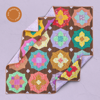 Folded colorful geometric patchwork quilt with floral patterns on a purple background, showcasing bright, warm tones and intricate design by Toad & Sew using the Garden Glow Quilt Pattern (Download).