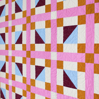 Geometric Glee Quilt Pattern (Download) by Straight Stitching featuring a bold geometric quilt design with pink strips blue and burgundy triangles and gold accents