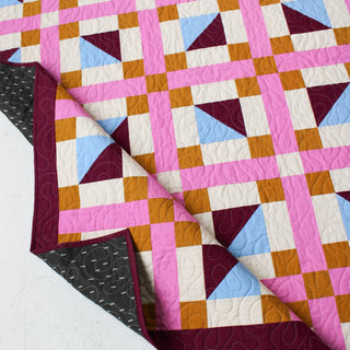Geometric Glee Quilt Pattern (Download) by Straight Stitching featuring a bold modern quilt with pink grid lines and colorful half square triangle blocks