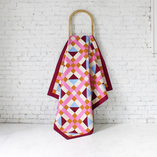 Geometric Glee Quilt Pattern (Download) by Straight Stitching, colorful geometric quilt with squares, rectangles, and half square triangles hanging on a wooden rack