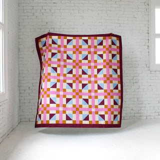 Geometric Glee Quilt Pattern (Download) by Straight Stitching, colorful geometric quilt with squares, rectangles, and half square triangles displayed on a white wall