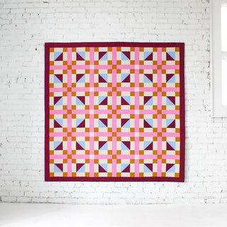 Geometric Glee Quilt Pattern (Download) by Straight Stitching featuring a bold geometric quilt with colorful squares rectangles and half square triangles on a white wall