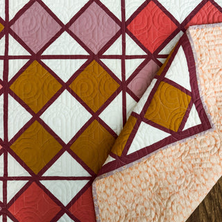 Closeup of the Harlequin Bloom Quilt Pattern (Download) by A Piece of Quiet Quilts, showcasing geometric floral blocks in warm autumn colors with detailed quilting stitches.