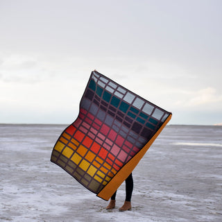Person holding a colorful quilt in a snowy landscape