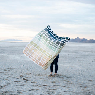 Person holding a large color swatch book in an open landscape with mountains in the background