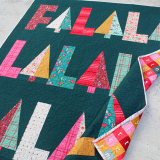 Fa-La-La Quilt Pattern (Download) by Patternly Collective featuring a colorful holiday quilt with bold letter blocks and a festive pieced border