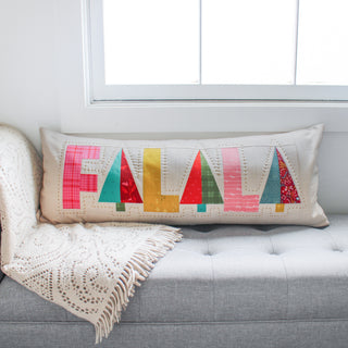 Fa-La-La Quilt Pattern (Download) by Patternly Collective featuring a colorful holiday quilted pillow with festive letter blocks on a gray sofa