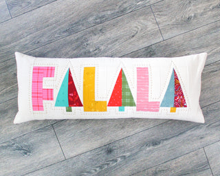 Fa-La-La Quilt Pattern (Download) by Patternly Collective featuring a colorful holiday quilted pillow with festive pieced letters on a white background