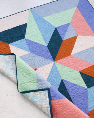 Geometric star quilt in soft pastel blues, greens, purples, and warm orange tones by Eudaimonia Studio using the Arete 8-Color Quilt Pattern (Download).