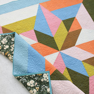 Colorful geometric quilt featuring intricate floral stitching and a dark floral fabric backing, showcasing the Arete 8-Color Quilt Pattern (Download) by Eudaimonia Studio.