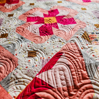 Close-up of a detailed quilt featuring warm mauve, pink, and mustard floral blocks with intricate circular quilt stitching, showcasing the Ixora Quilt Pattern (Download) by Thai Charm.