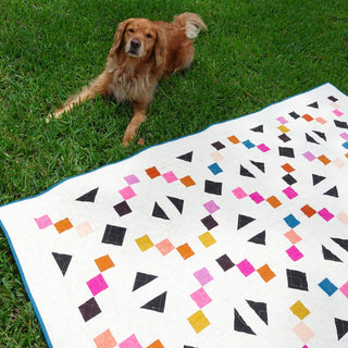 Keystone Quilt Pattern (Download) by Homemade Emily Jane featuring colorful geometric shapes on a white quilt displayed on grass beside a friendly dog