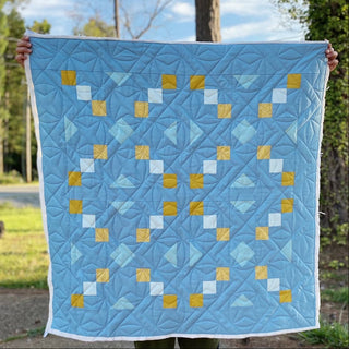 Keystone Quilt Pattern (Download) by Homemade Emily Jane featuring a modern geometric quilt with blue tones and gold accents in a balanced symmetrical design