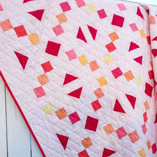 Keystone Quilt Pattern (Download) by Homemade Emily Jane featuring a modern geometric quilt in soft pink with red orange and yellow shapes.