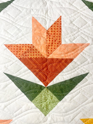 Close-up of a fabric floral quilt block in orange and green shades on a white background from Shadow Valley Quilts, showcasing the Lilies on Parade Quilt Pattern (Download).
