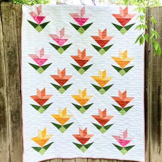 Bright quilt with geometric tulip blocks in pink, orange, and yellow on white background, featuring modern quilting by Shadow Valley Quilts using Lilies on Parade Quilt Pattern (Download).