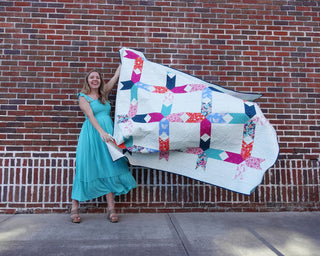 Limelight Quilt Pattern (Download) by Homemade Emily Jane featuring a modern geometric quilt with colorful abstract blocks and crisp white negative space held outdoors by a smiling woman
