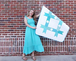 Homemade Emily Jane Limelight Quilt Pattern (Download) featuring a modern geometric quilt in turquoise and white held by a smiling woman against a brick wall