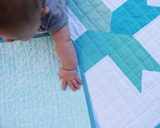 Limelight Quilt Pattern (Download) by Homemade Emily Jane featuring a baby resting on a turquoise geometric quilt with white negative space and grid quilting