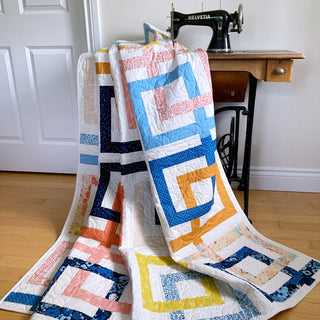 Colorful geometric quilt with interlocking ribbon-like squares draped over a vintage sewing machine, showcasing the Line Dance Quilt Pattern (Download) by Penny Spool Quilts.
