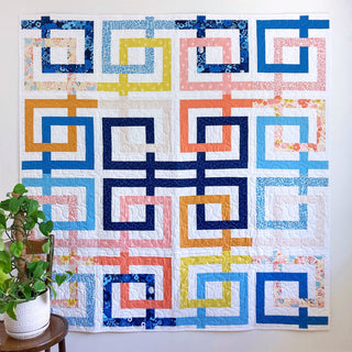 Colorful quilt with interlocking ribbon-like loops in blue, pink, yellow, and orange tones, showcasing the Line Dance Quilt Pattern (Download) by Penny Spool Quilts.