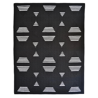 Living Room Quilt Pattern by Sewn flat lay: black quilt with repeating white geometric shapes including hexagons, triangles, and striped diamonds.