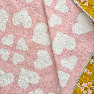Close-up of a pink and white quilt featuring heart shapes and intricate stitching, showcasing the Lovelace Quilt Pattern (Download) by The Dandy Patch.
