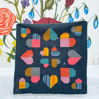 Colorful geometric heart blocks arranged on a dark background in a small quilt, showcasing the Lovelace Quilt Pattern (Download) by The Dandy Patch.