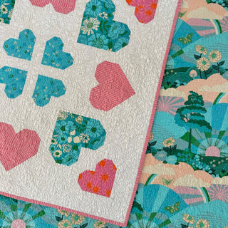 Close-up of a handmade quilt featuring heart-shaped and floral block patterns in pink, teal, and white, showcasing intricate quilting by The Dandy Patch, perfect for the Lovelace Quilt Pattern (Download).