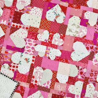 Close-up of a colorful scrappy quilt featuring heart and geometric patchwork in pink, red, and white tones, showcasing the Lovelace Quilt Pattern (Download) by The Dandy Patch.