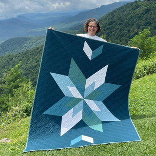 Max Patch Quilt Pattern by Hampton Quilt Studio cover: woman holding a large teal and white geometric star quilt outdoors with mountain landscape behind her.