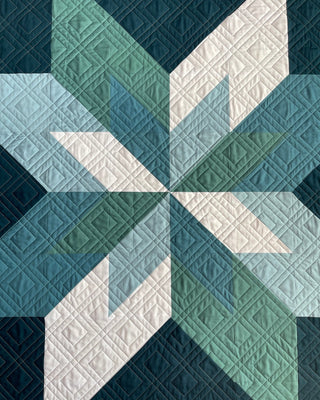 Max Patch Quilt Pattern by Hampton Quilt Studio flat lay: overhead view of geometric star quilt in teal, navy, and white showing detailed quilting stitches.
