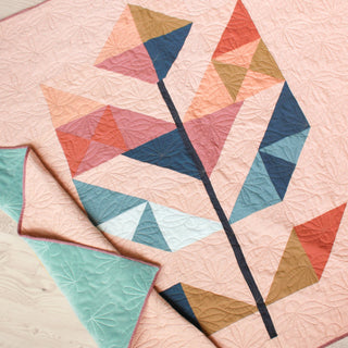 Close-up of a modern pieced quilt with geometric shapes in muted pinks, blues, and browns, featuring floral quilting by Month of May Quilting for May Quilt Pattern (Download).